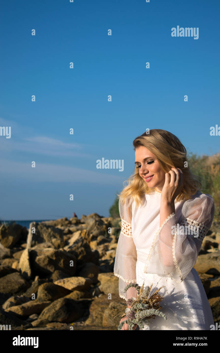 Smiling woman in white dress on background of field and blue sky. Bride Stock Photo