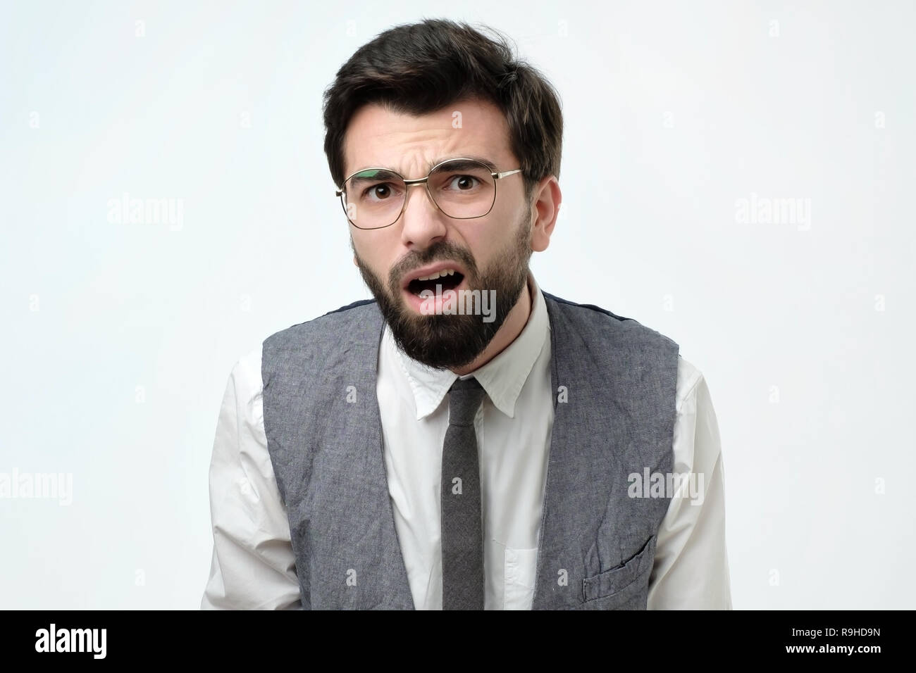 Suspicious bearded man looks doubtfully, being indecisive, makes grimace, tries to find solution. Stock Photo