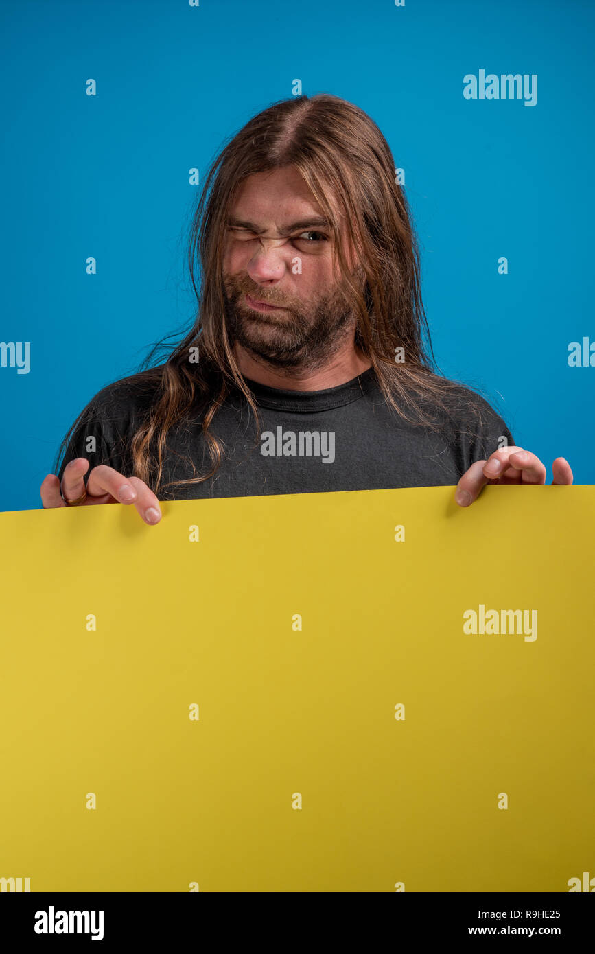Male portrait displaying a funny wink sign while holding a yellow banner. Copyspace available for advertise message or information Stock Photo