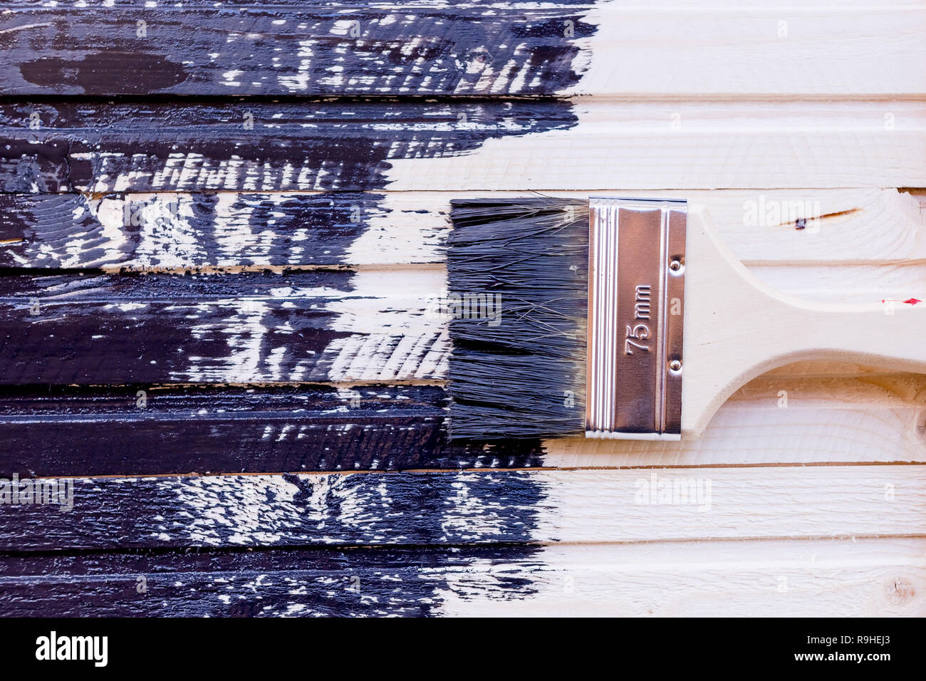 Half painted wooden surface. Black color. Varnishing natural wood with paint brush.Painting natural wood wall with brush.putting layer of clear lacquer on surface of beech top table. wood maintenance oil-wax Stock Photo