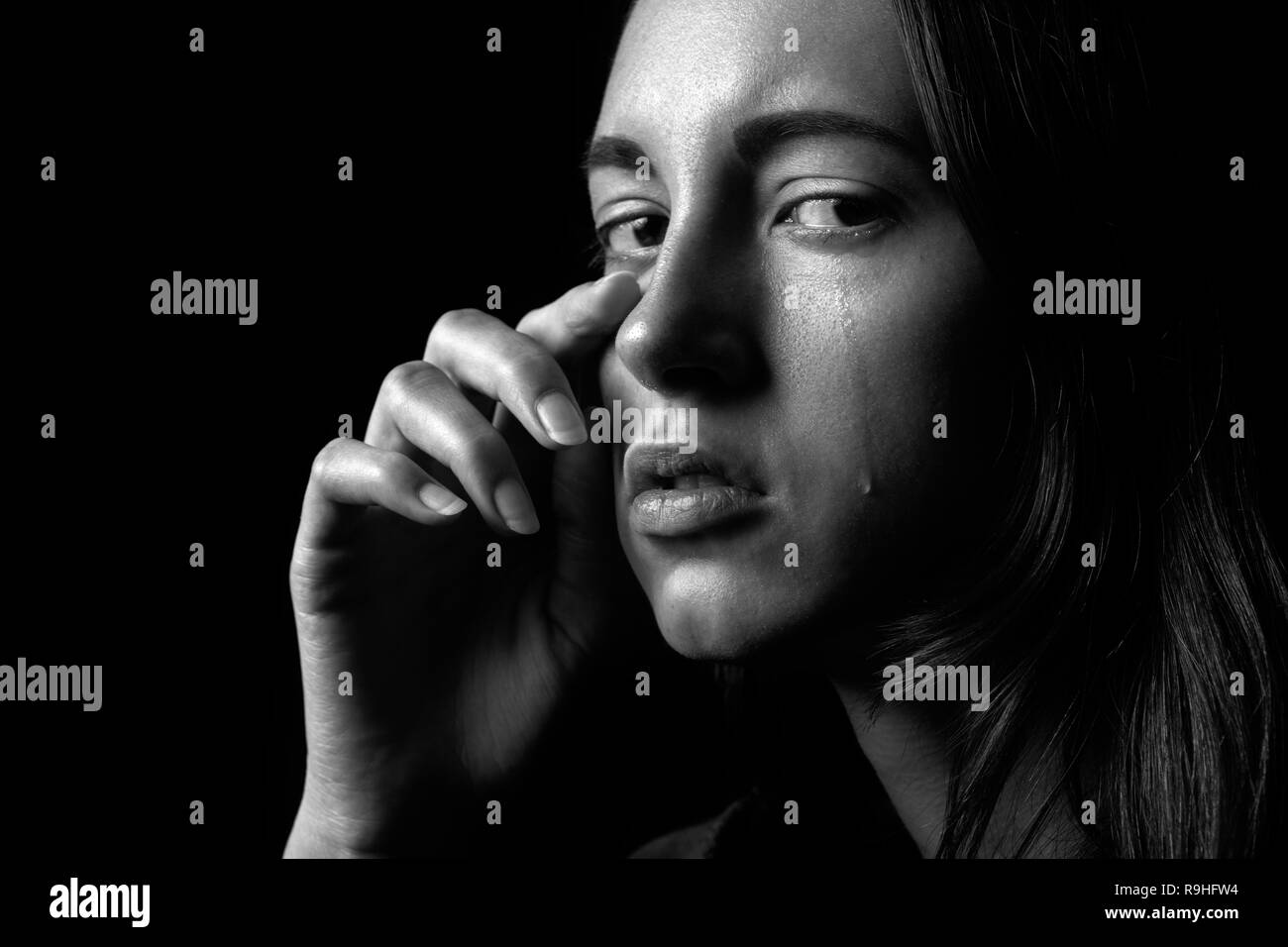 sad woman crying on black background, looking at camera, closeup portrait Stock Photo