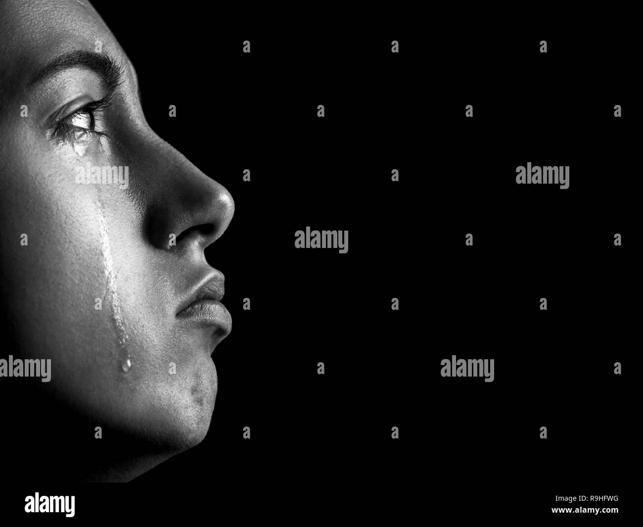 sad woman crying, looking up on black background with copy space, closeup portrait, profile view, monochrome Stock Photo
