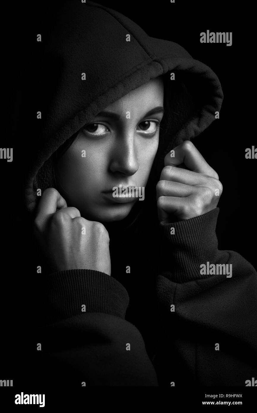 scared girl in hood looking at camera on black background Stock Photo