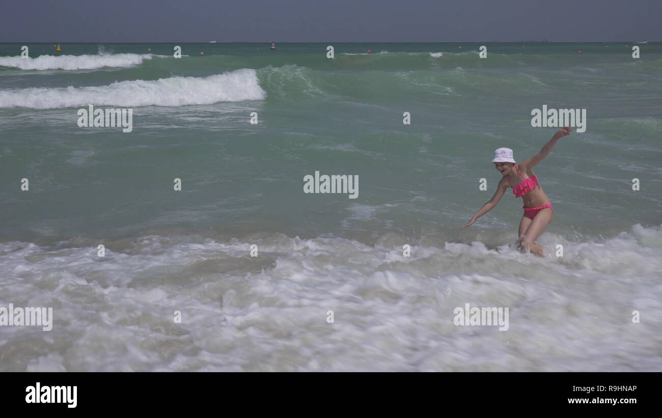 Teenage girl in a bathing suit happily jumps in waves of Persian Gulf on beach of Dubai Stock Photo