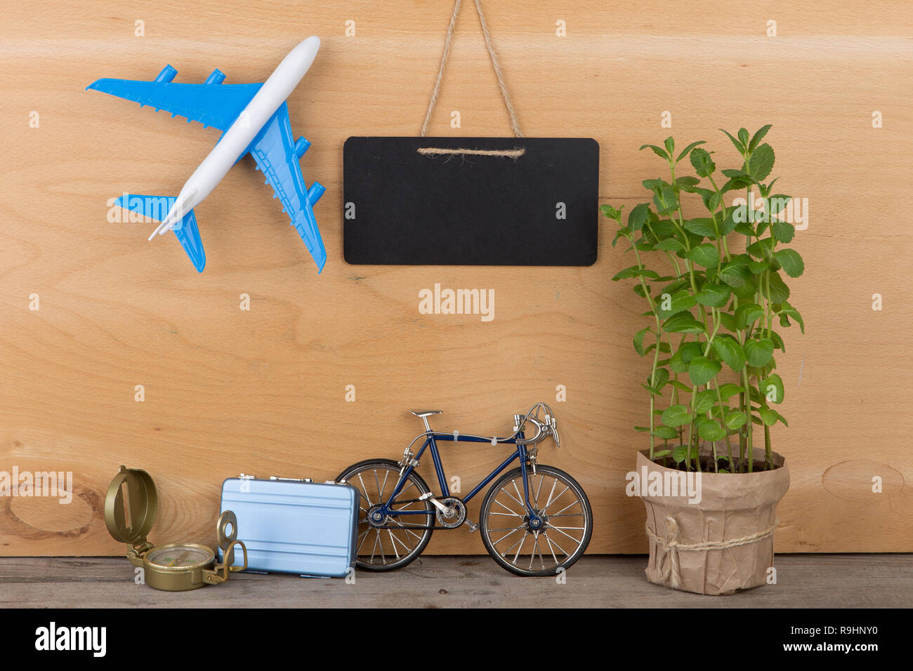 Travel time concept - blank blackboard, airplane model, little bicycle and suitcase, compass on wooden background Stock Photo
