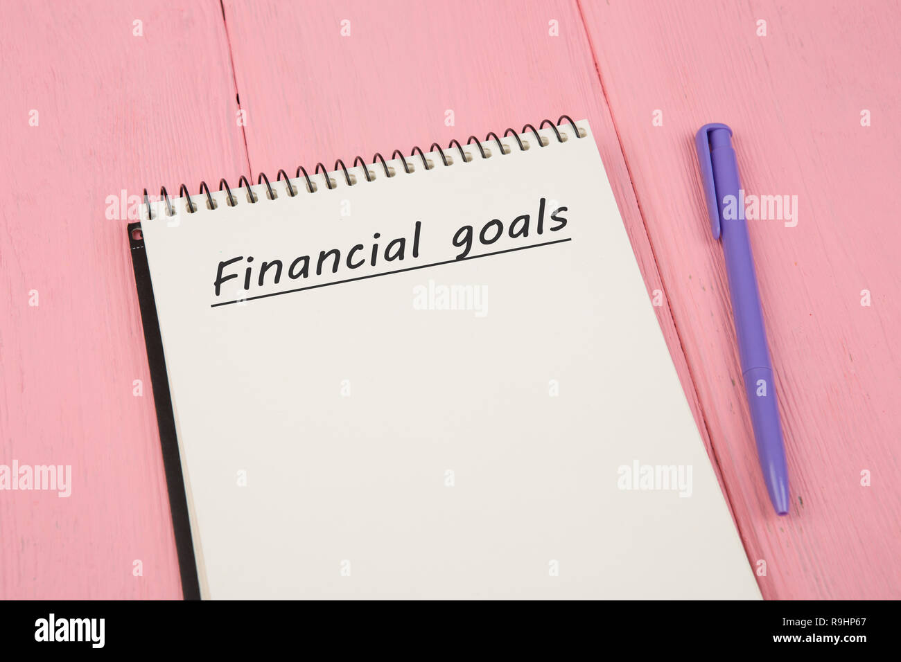 Notepad with text 'Financial goals' and pen on pink wooden table Stock Photo