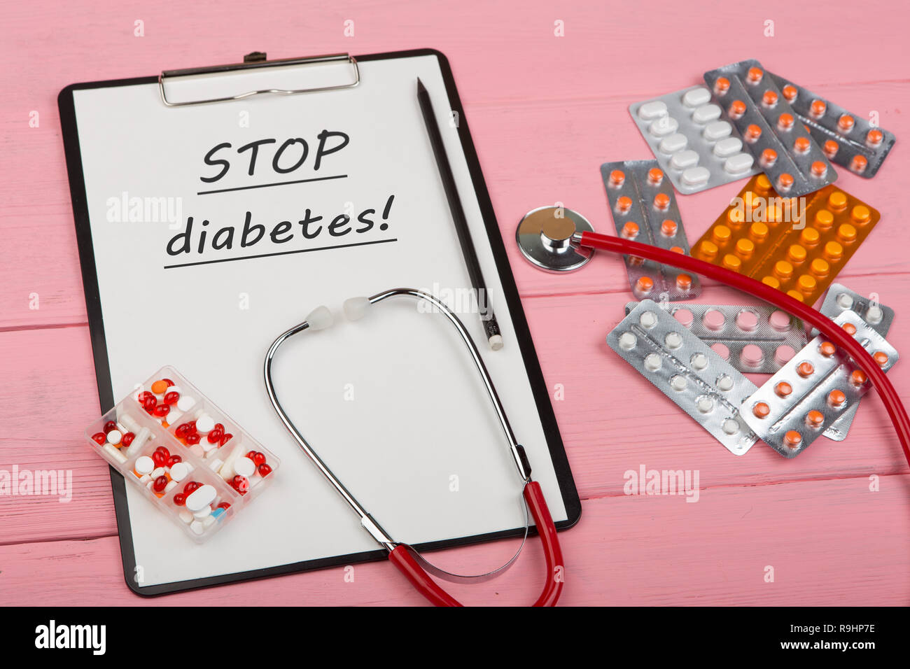 Doctor workplace with clipboard and text 'STOP diabetes!', medicine red stethoscope and pills on pink wooden table. Medication prescription. Health ca Stock Photo