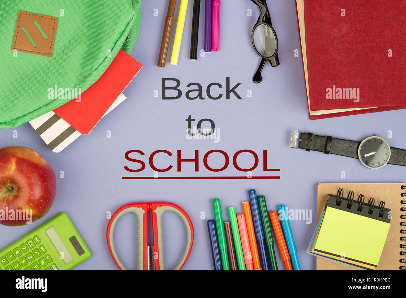 Backpack and school supplies: notepad, felt-tip pens, eyeglasses, scissors, calculator, book, watch on blue paper background with text 'Back to school Stock Photo