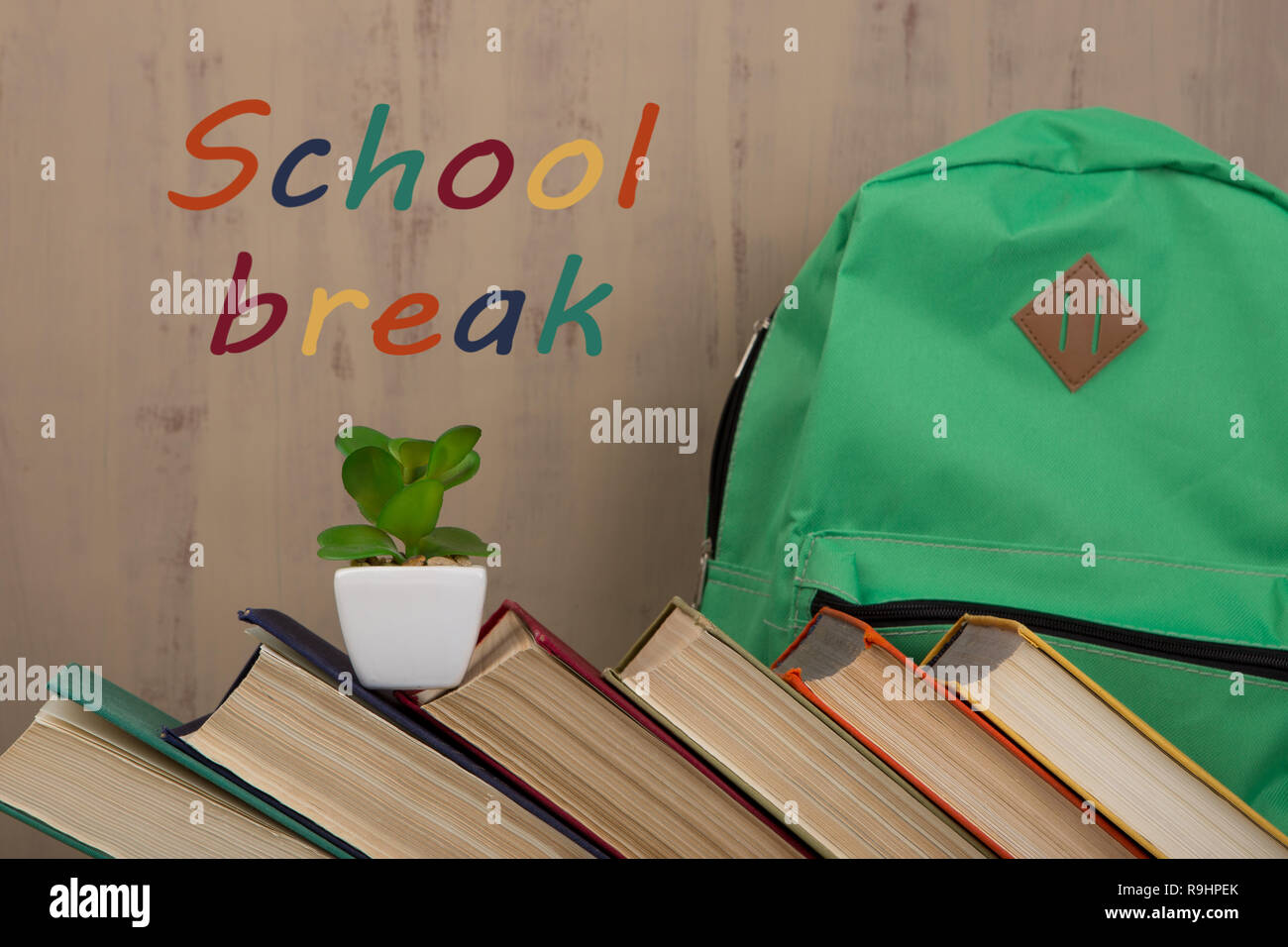 Back to school and education concept - colorful hardback books and green backpack on brown background with text 'School break' Stock Photo