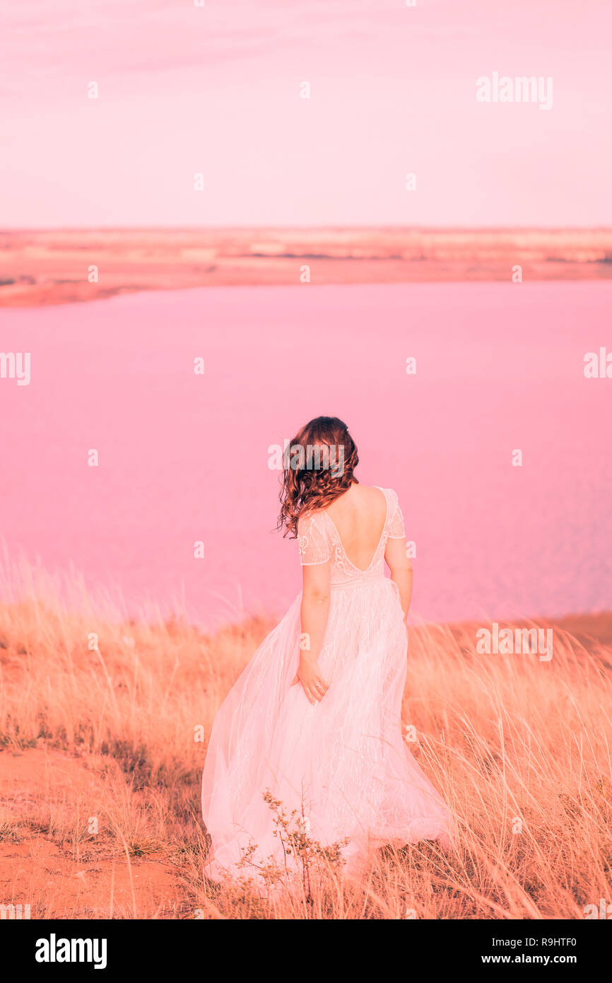 Woman bride in wedding dress near the lake, from behind. The concept of fashion colors 2019, living coral Stock Photo