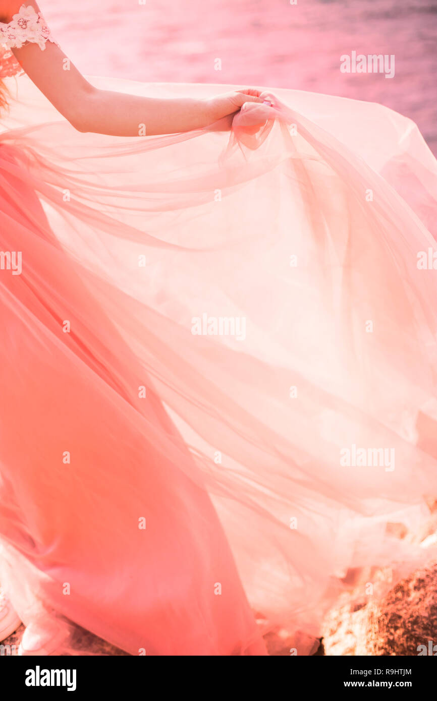 The bride is wearing a wedding dress gently coral color on the sea. Beautiful tulle. The concept of fashion colors 2019 Stock Photo