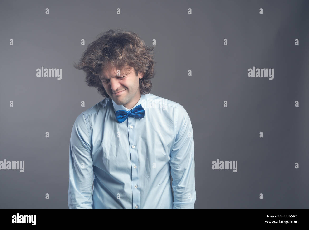 Portrait of unhappy hophead man standing and looking aside with melancholy. Isolated on grey background wearing blue shirt and bow tie. Hunched should Stock Photo