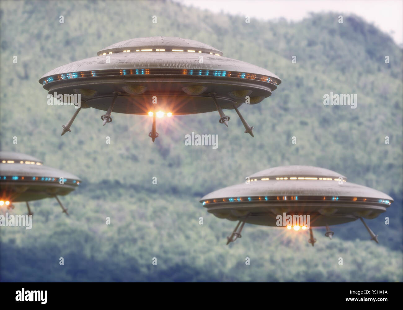 Three unidentified flying objects over a forest with trees and mountains behind. Stock Photo