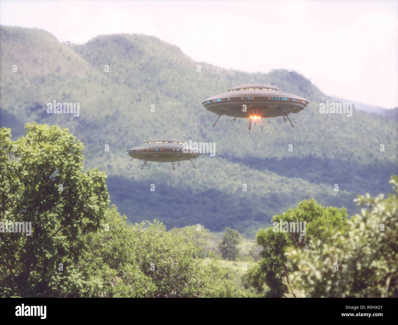 Two unidentified flying objects over a forest with trees and mountains behind. Stock Photo