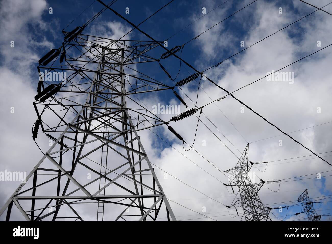 Steel transmission tower and high voltage electrical power lines against blue sky and clouds in