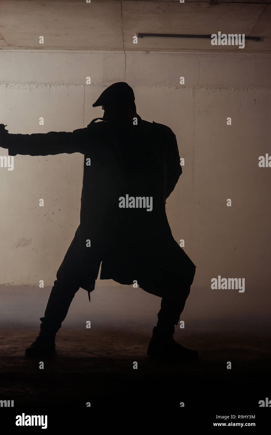 Silhouette of a man standing still with a gun in his hands Stock Photo