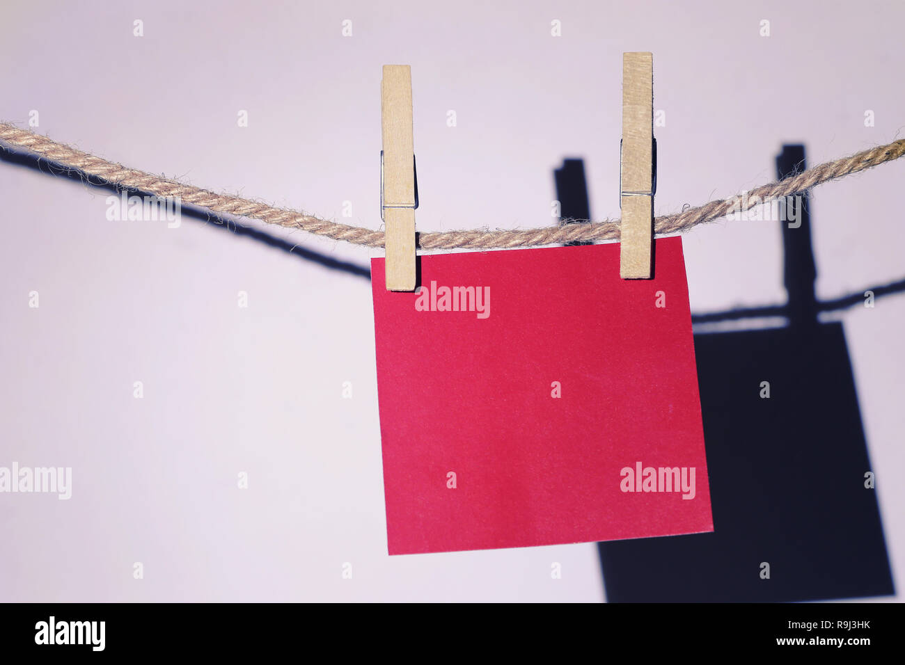 Red note paper hanging on rope on white wall and have clipping paths. Stock Photo