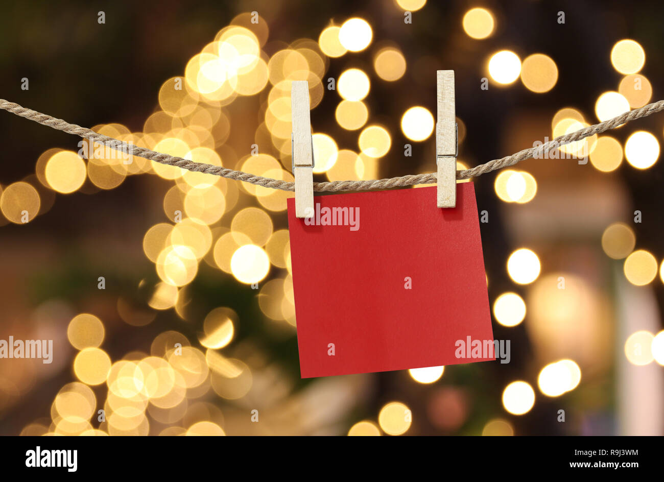 Blank red paper notes hanging on clothesline for design in Christmas Day on bokeh light background,Notepad for design ideas for Important day. Stock Photo