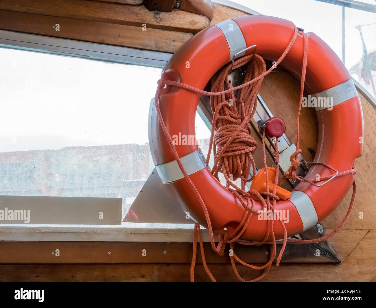 Safe water support aid circle with rope. Rescue red life buoy on wooden background of ship or boat. Helpful object. No people. Stock Photo