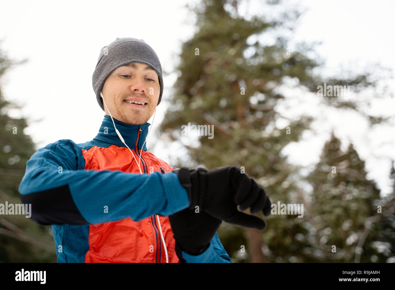 Runner wearing warm sporty clothes in headphones looks at a modern smart clock Stock Photo