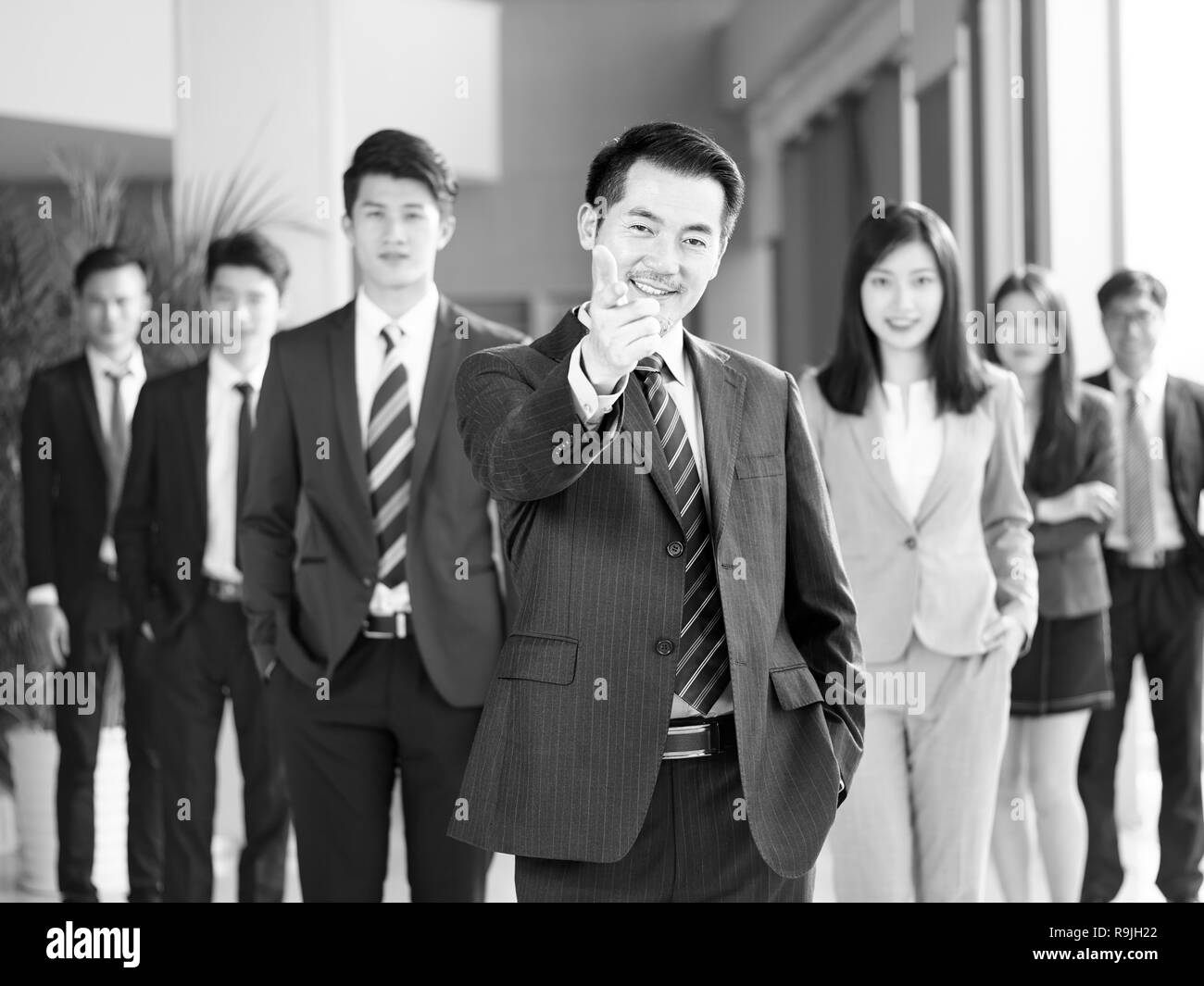 portrait of a team of successful asian businessmen and businesswomen, pointing and looking at camera smiling, black and white. Stock Photo