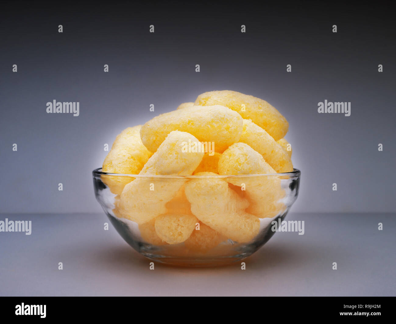 Yellow Corn Puffs in a Glass Bowl Isolated On Dark Gray Background