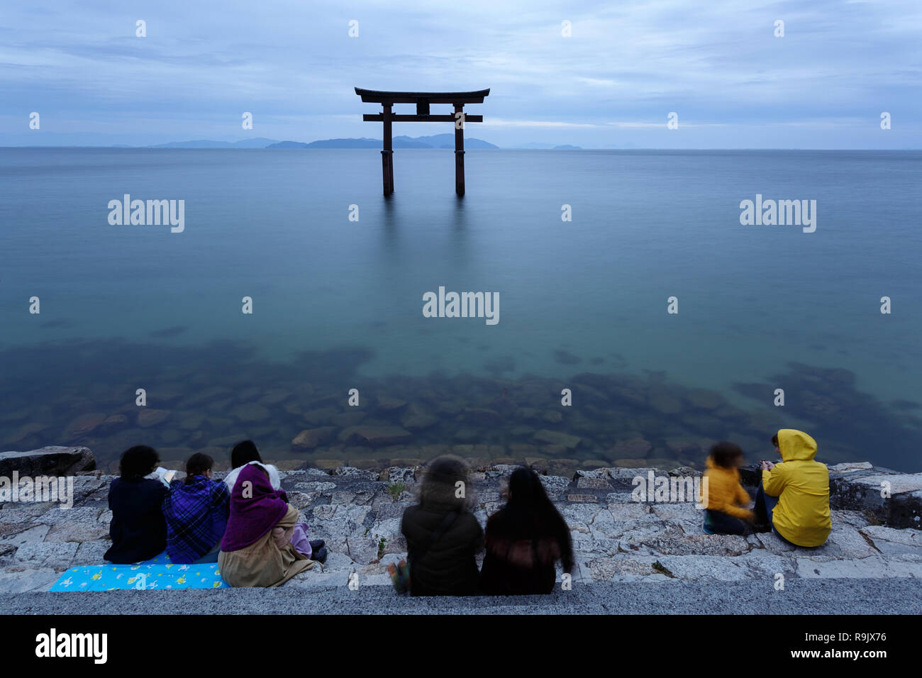 People sitting on steps on the lake looking at Torii gate on water, Shirahige Jinja Torii, lake Biwa near Kyoto, Japan Stock Photo