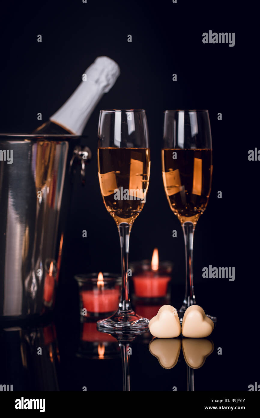 Champagne bottle in bucket, two wine glasses and two heart-shaped chocolates and candles on black background. Love, Valentines day concept Stock Photo