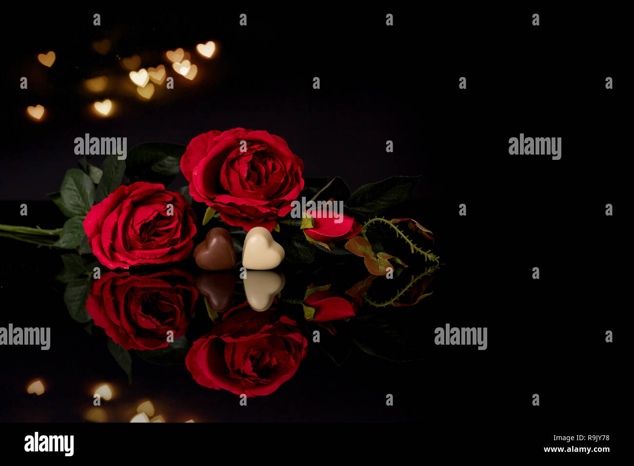 Valentines day greeting card with red roses and heart shaped chocolate with lights on the black background Stock Photo