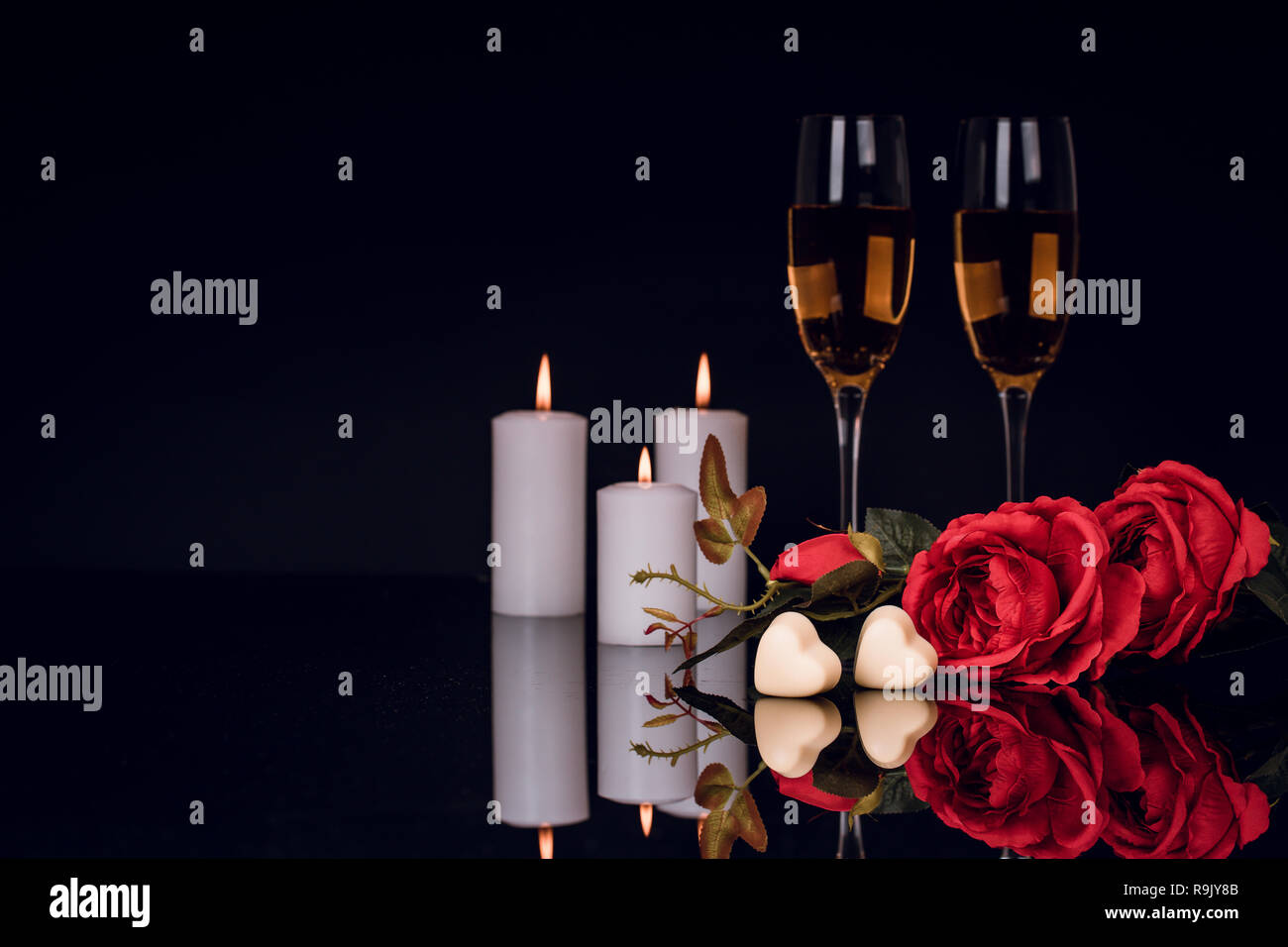 Two glasses of champagne, roses, candles and two heart shape chocolates on black background. Love, Valentines day concept Stock Photo