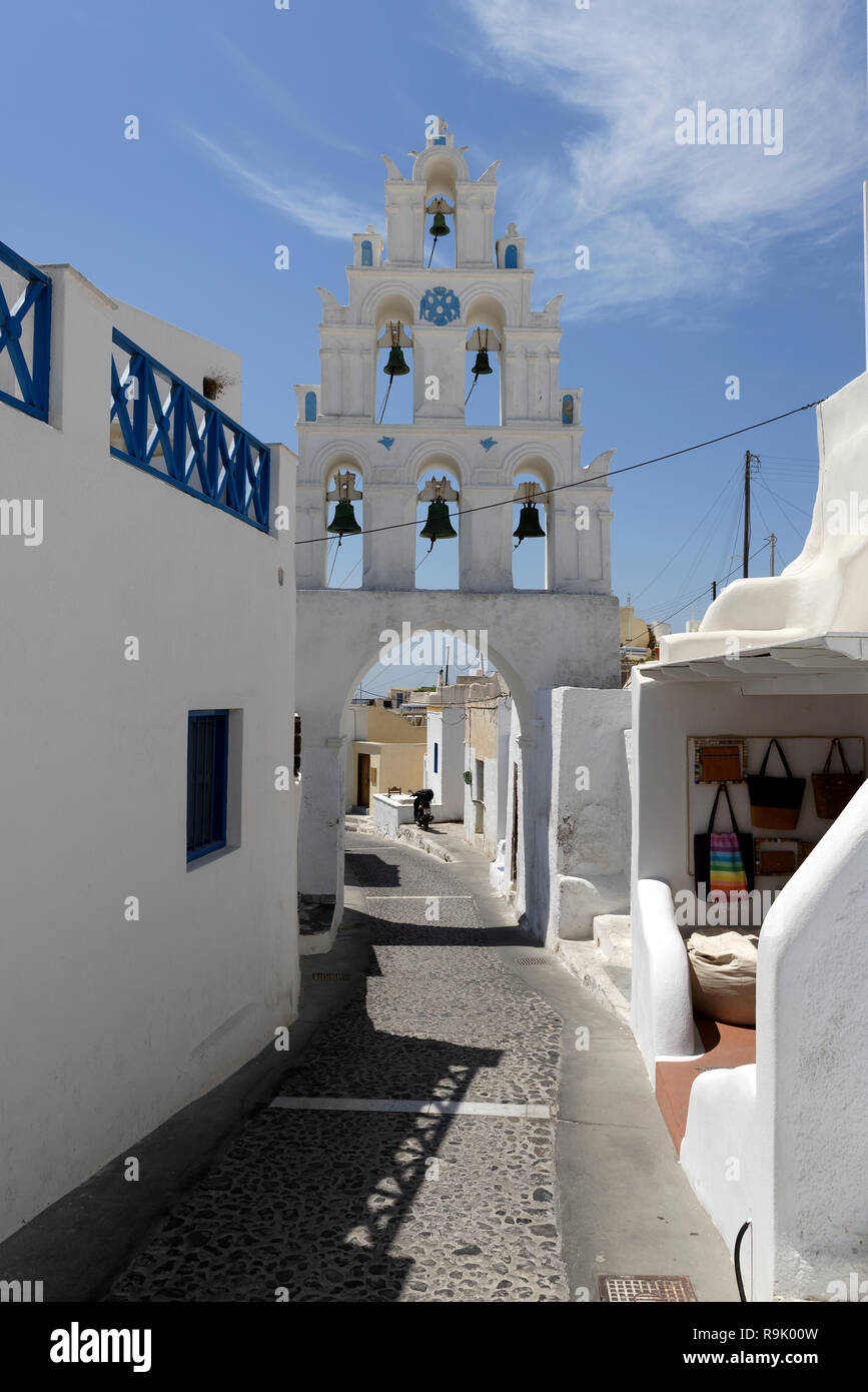 Three-tiered whitewashed Bell tower bridges a cobblestone lane Megalochori, Santorini, Greece. The bell tower is part of the church of the Saints (Agi Stock Photo