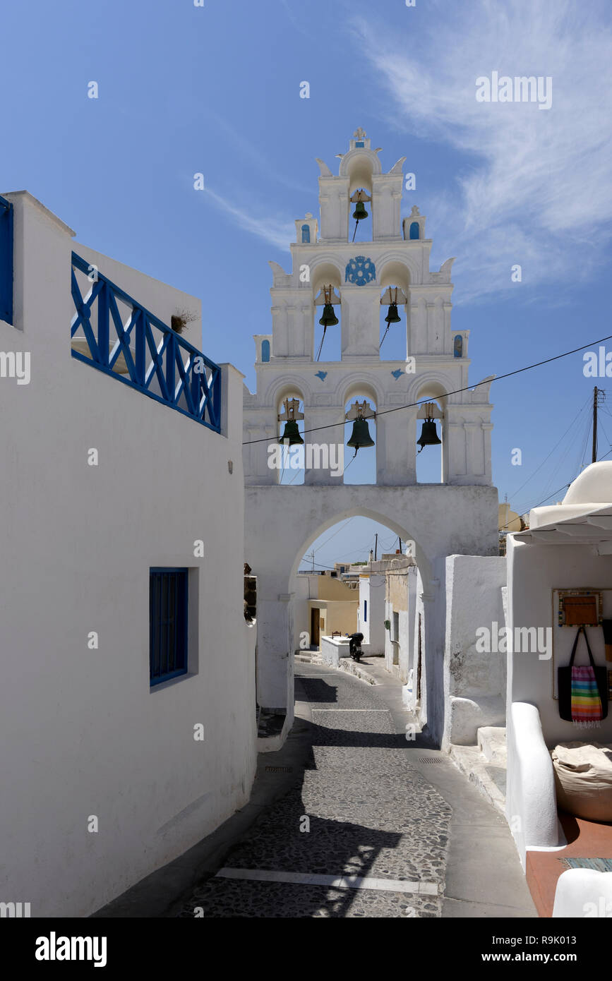 Three-tiered whitewashed Bell tower bridges a cobblestone lane Megalochori, Santorini, Greece. The bell tower is part of the church of the Saints (Agi Stock Photo