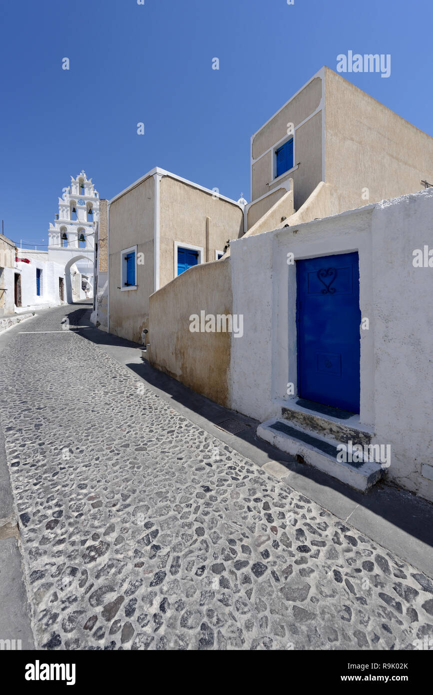 Three-tiered whitewashed Bell tower bridges a cobblestone lane Megalochori, Santorini, Greece. The bell tower is part of the church of the Saints (Agi Stock Photo