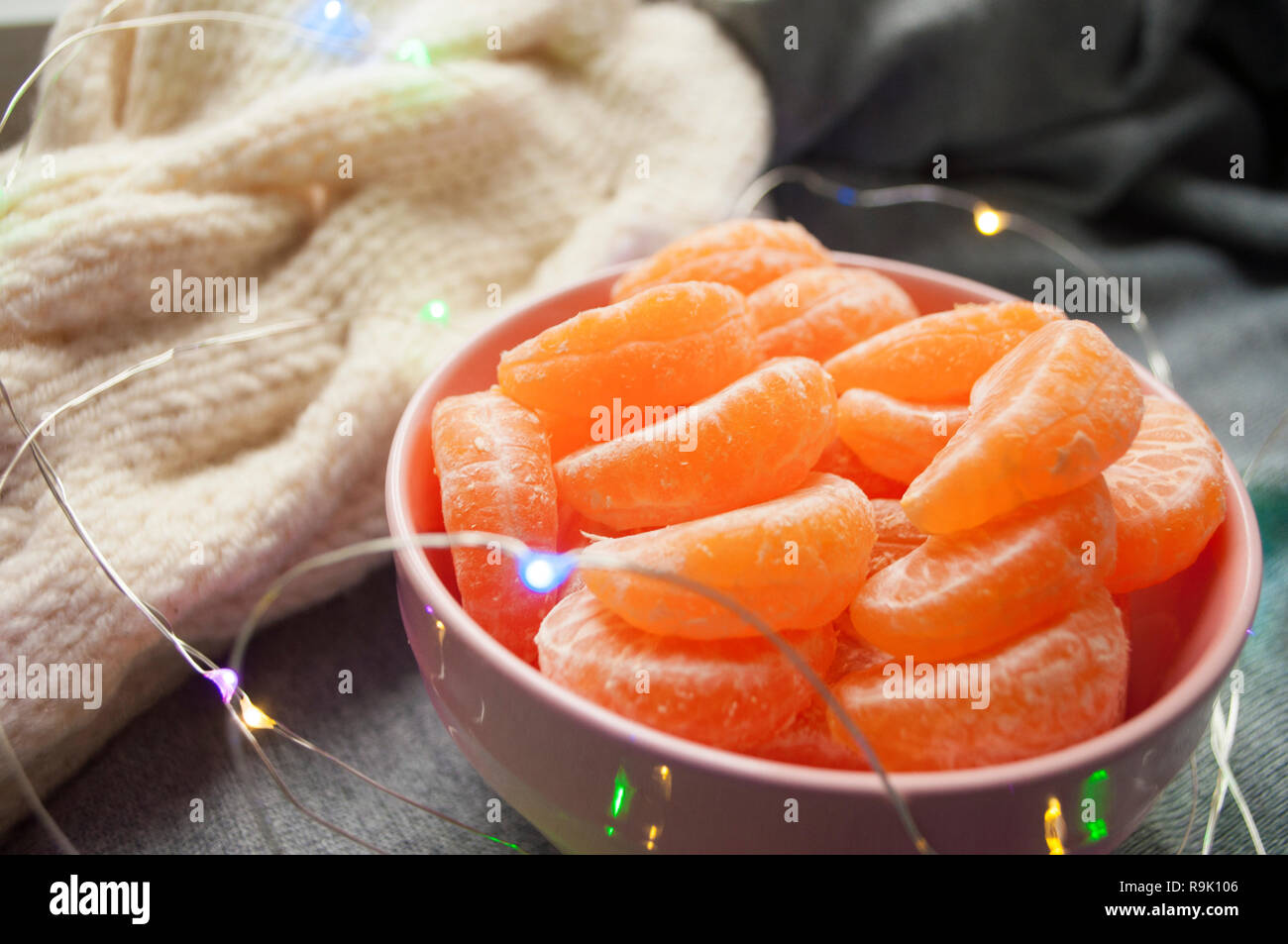 Pink bowl full of peeled sweet tangerines on grey background with garland lights. Stock Photo