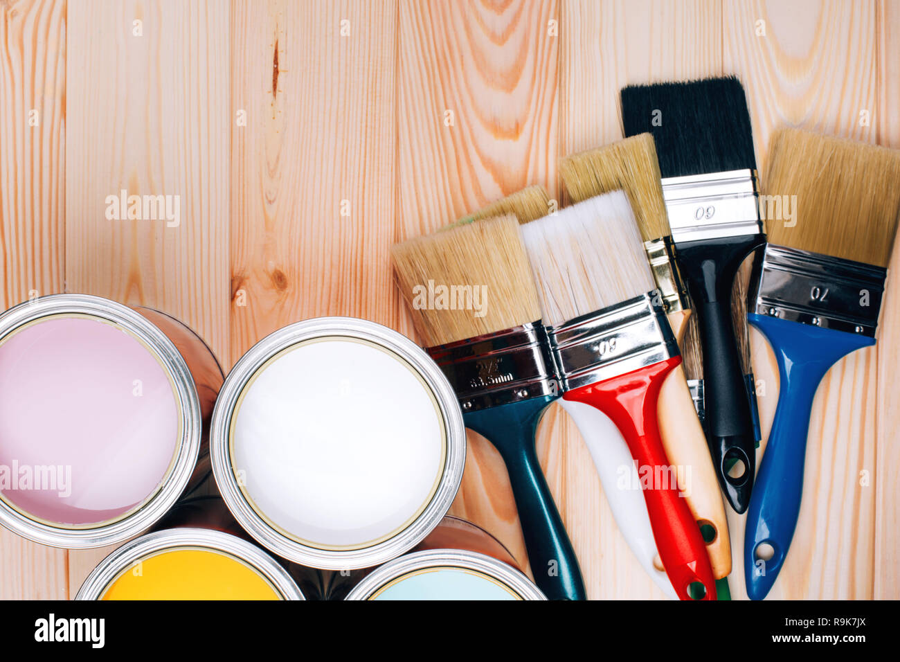Four open cans of paint with brushes on natural wooden background. Yellow, white, pink, turquoise colors. Renovation concept. Stock Photo