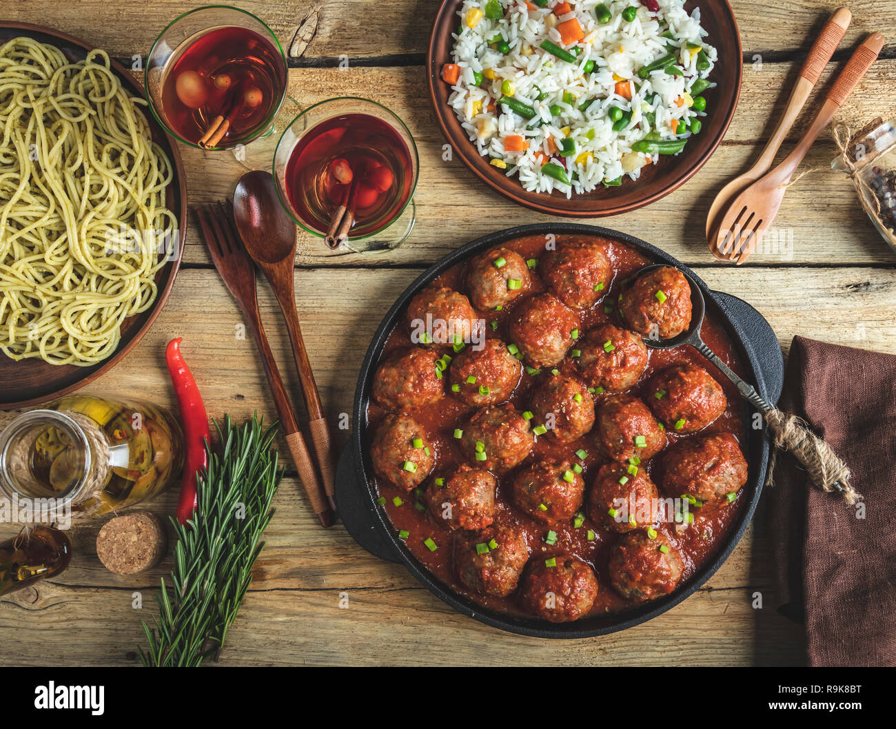 Homemade meatballs in tomato sauce. Frying pan on a wooden surface, rice with vegetables, pasta Stock Photo