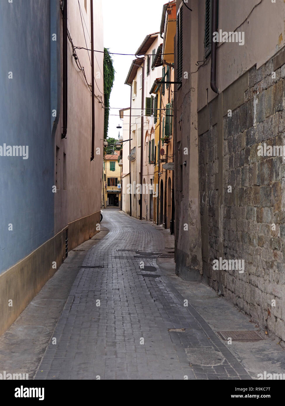 typical winding narrow Tuscan paved street in shadow with plain blue wall and stonework, downpipes and shuttered windows in Pisa, Italy Stock Photo