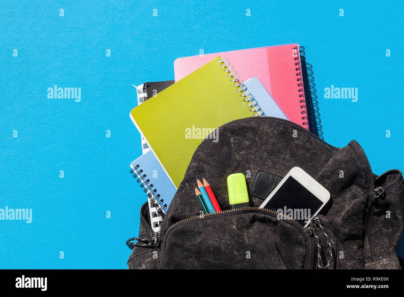 Spiral notebooks coming out of a black schoolbag, penciles and mobile phone Stock Photo
