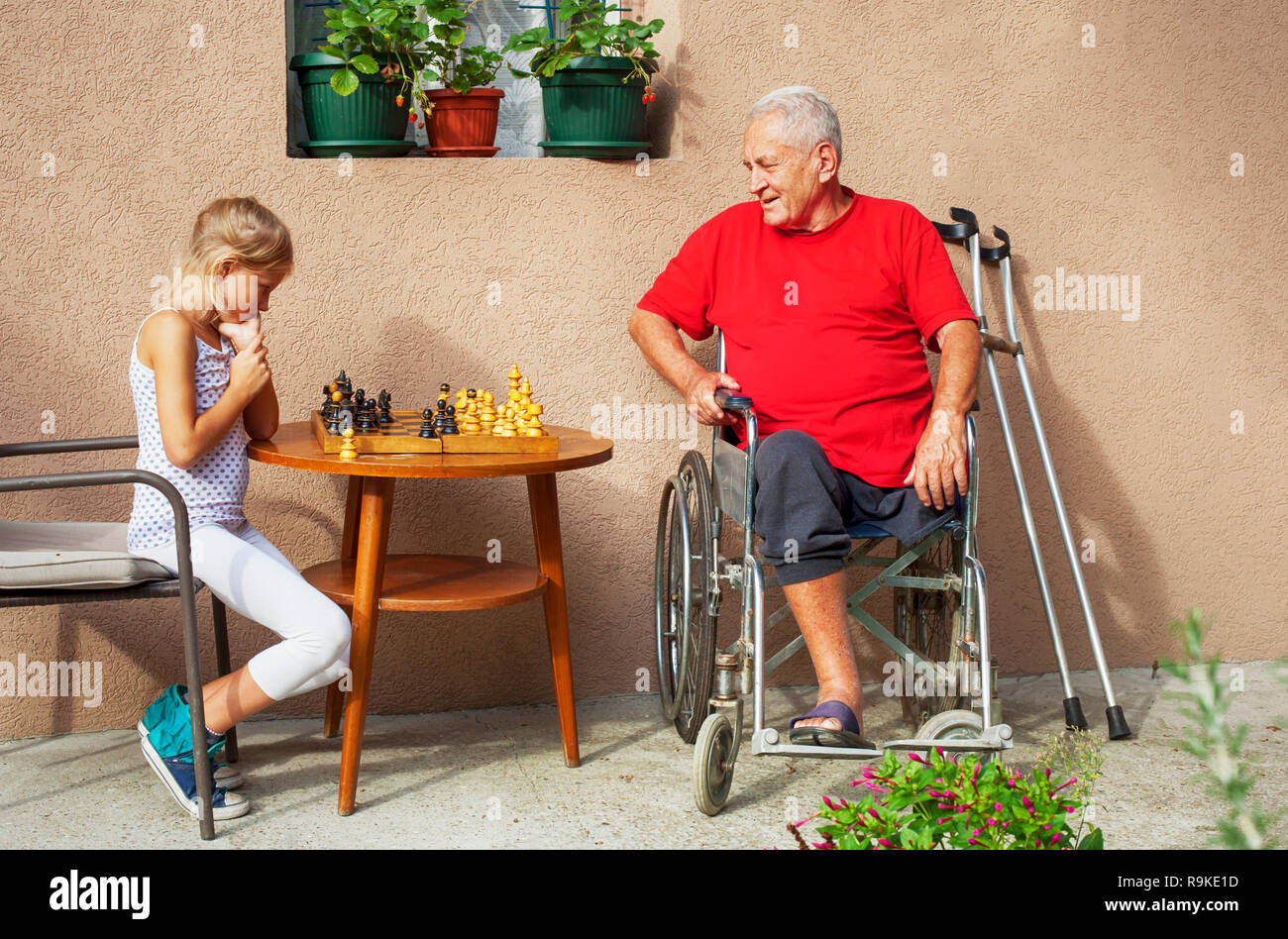 Disabled Senior and his beautiful young granddaughter playing chess and smiling outside Stock Photo