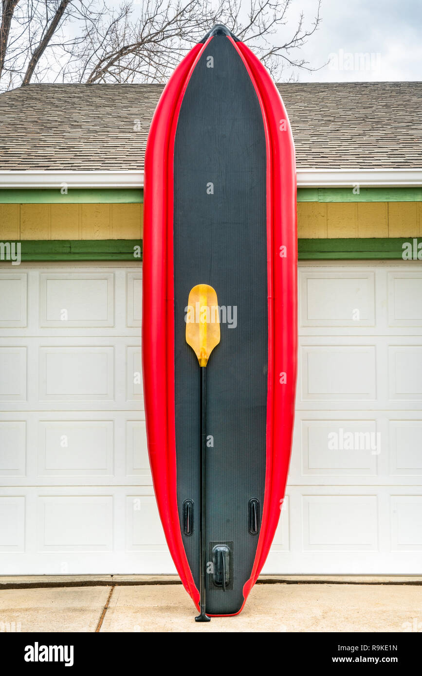 whitewater inflatable stand up paddleboard with a paddle leaned against house wall Stock Photo