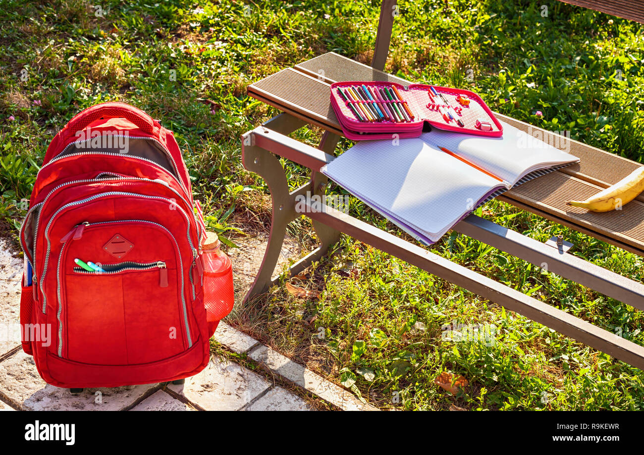 Modern red school bag and pencil box with notebook on the bench in the