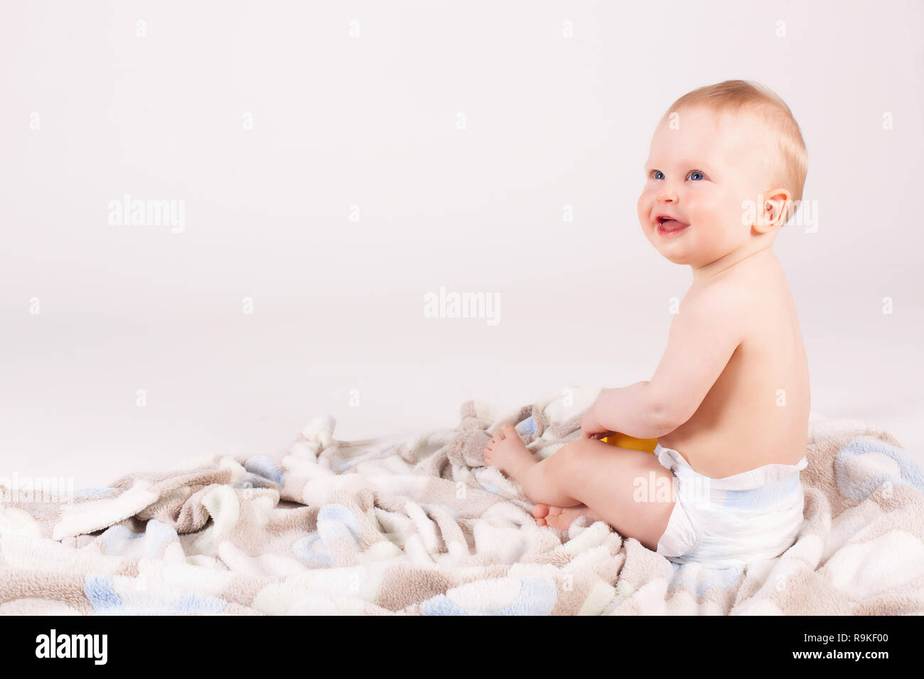 Adorable happy little boy smiling and sitting on a blanket, studio shoot. Stock Photo