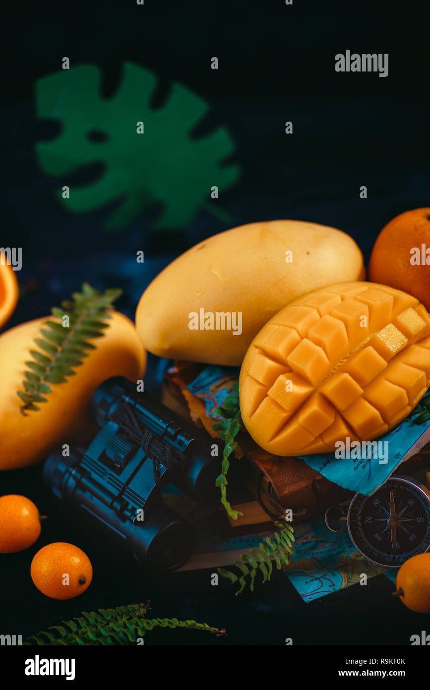 Mango close-up with oranges, kumquat, and other tropical fruits. Dark background with copy space. Traveling and discovery of exotic fruits concept. Stock Photo