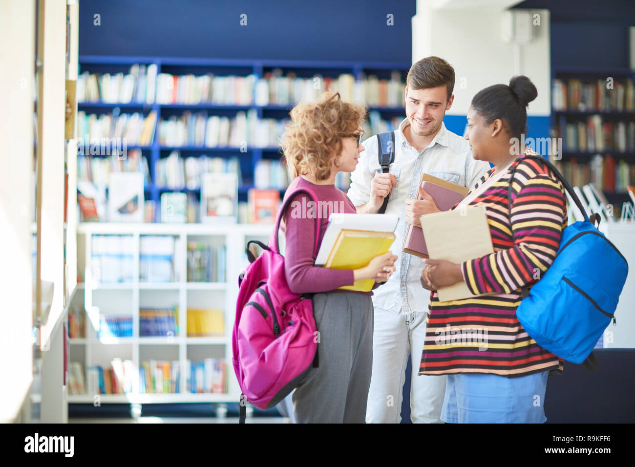Cheerful friends discussing literature in library Stock Photo