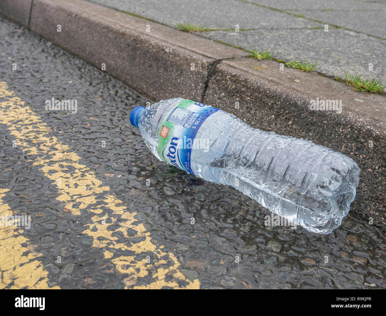 Empty PTFE plastic mineral water bottle discarded in urban road gutter. For plastic pollution, environmental pollution, war on plastic waste. Stock Photo