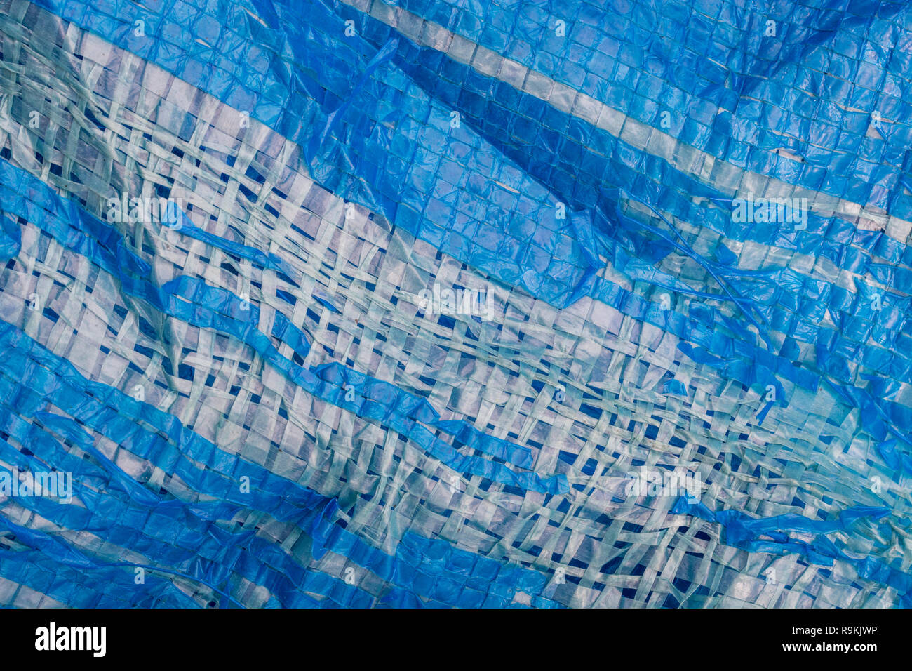 Macro-photo of very worn blue cheap Poly-Tarpaulin - exposed inner woven plastic fabric laminated with blue LDPE / Low-density Polyethylene. Stock Photo