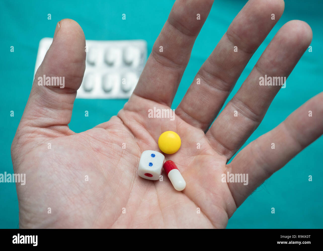 Left hand supports a few pills and a dice, conceptual image Stock Photo
