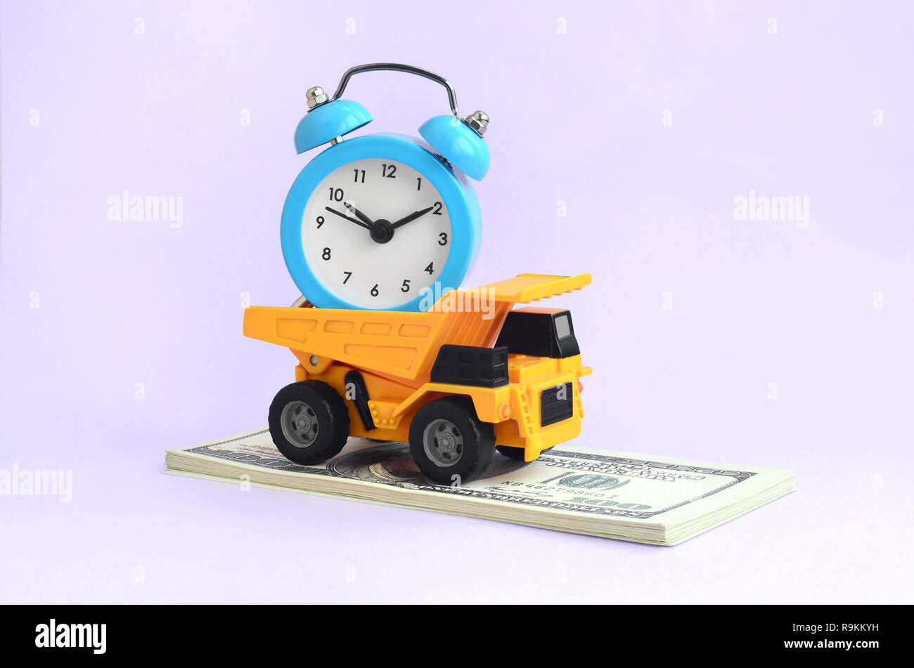 A dump truck loaded with an alarm clock is on a wad of dollar bills