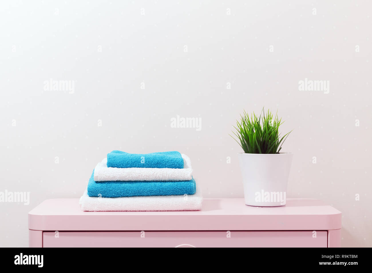 On a pink dresser there is a pile of towels and a home plant stands Stock Photo