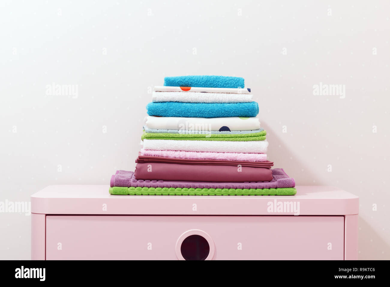 On the dresser there is a stack of clean ironed bed linen, folded colored towels. Stock Photo